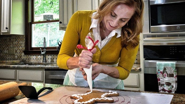 Woman decorating gingerbread man with icing.